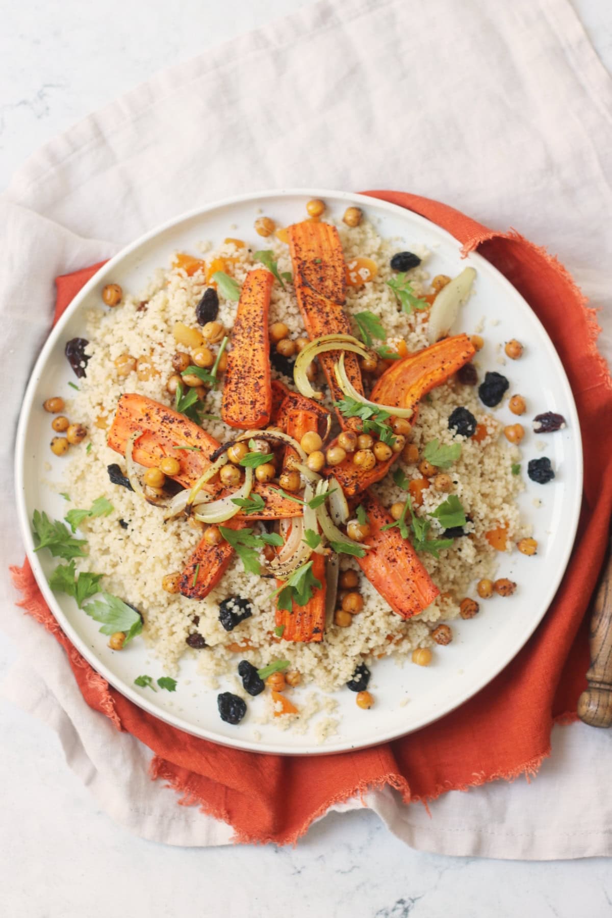 Vegan Warm Moroccan Spiced Couscous with Roasted Carrots on a white plate on top of an orange napkin