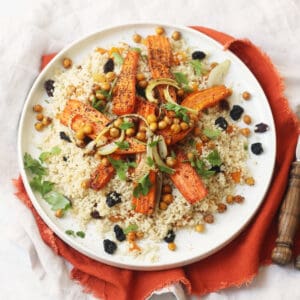 Vegan Warm Moroccan Spiced Couscous with Roasted Carrots on a white plate on top of an orange napkin