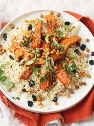 Vegan Warm Moroccan Spiced Couscous with Roasted Carrots on a white plate on top of an orange napkin