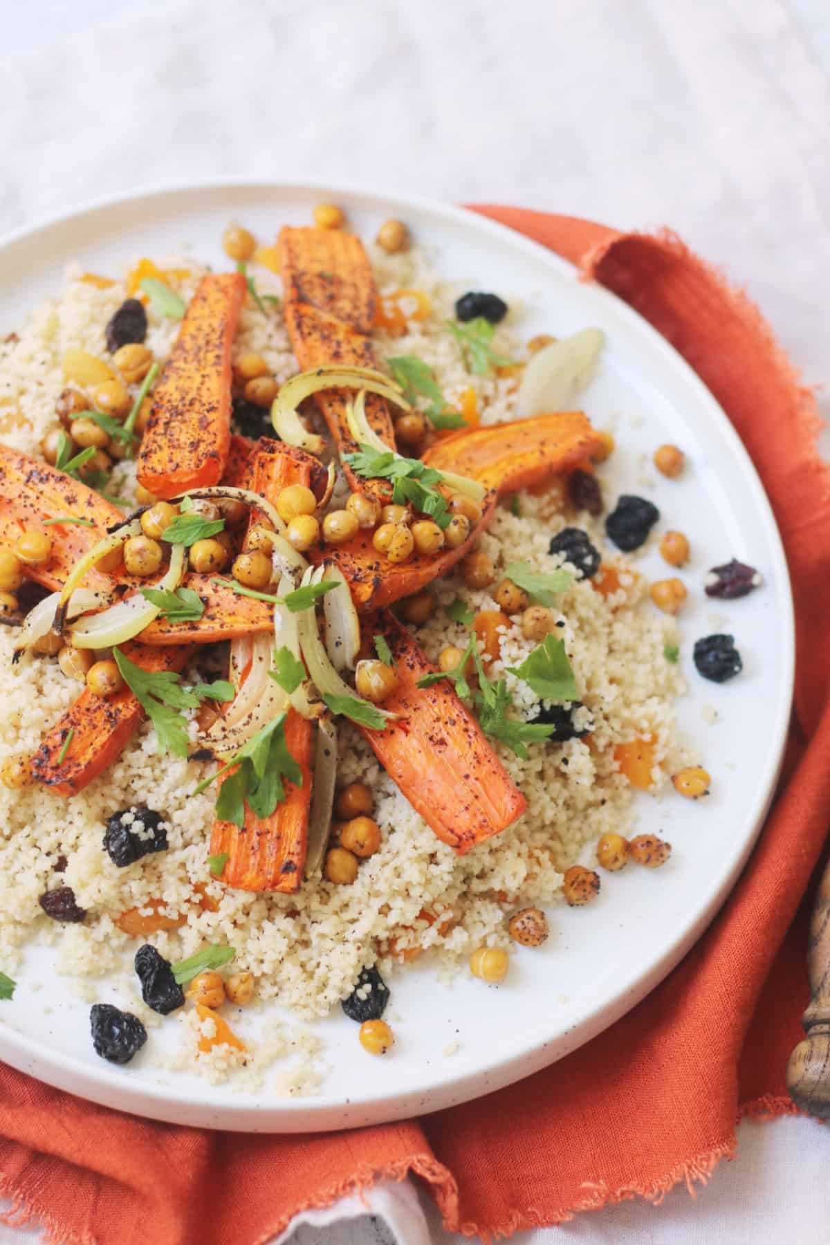 Vegan Warm Moroccan Spiced Couscous with Roasted Carrots on a white plate on top of an orange napkin