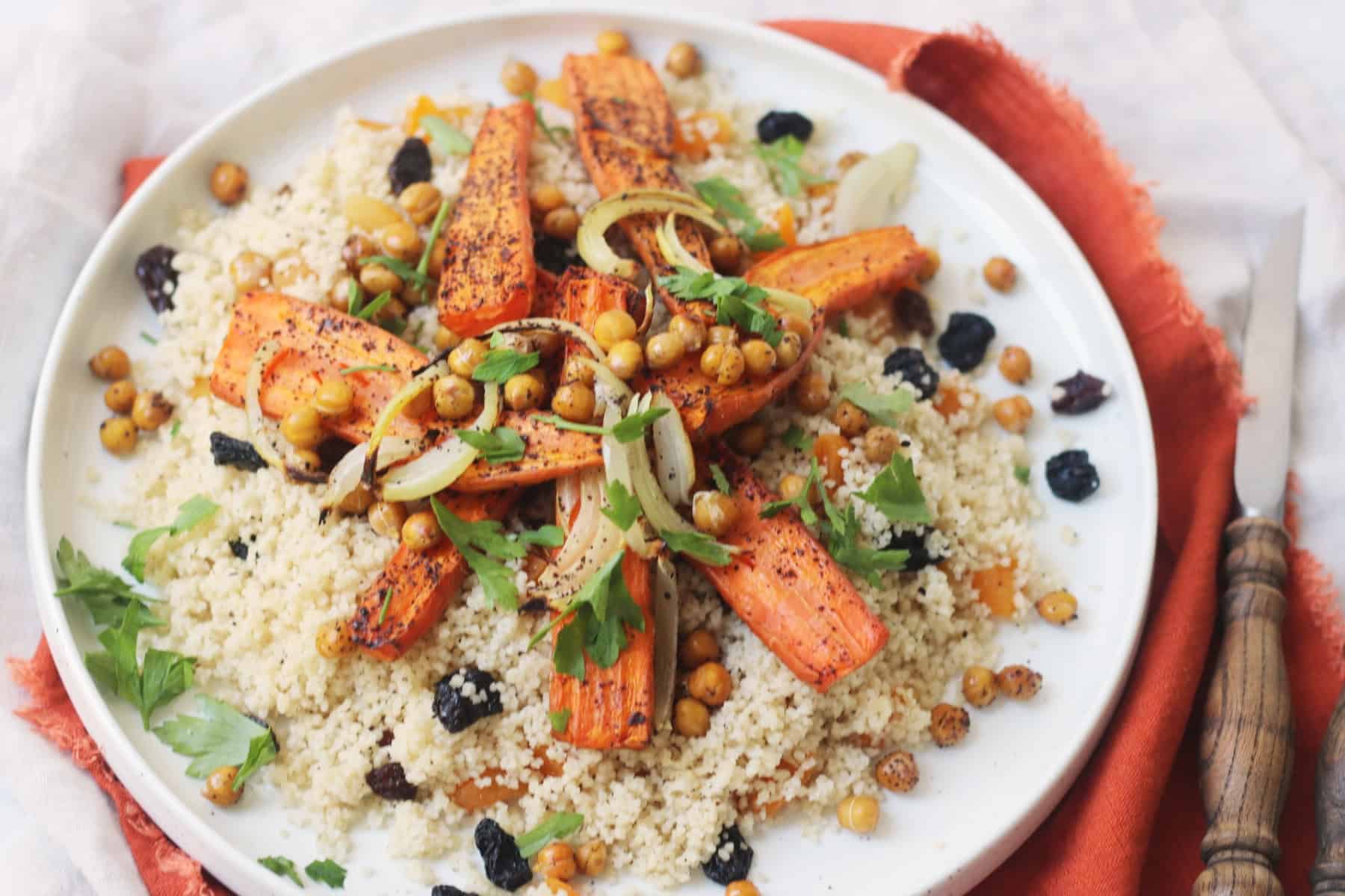 Vegan Warm Moroccan Spiced Couscous with Roasted Carrots on a white plate on top of an orange napkin