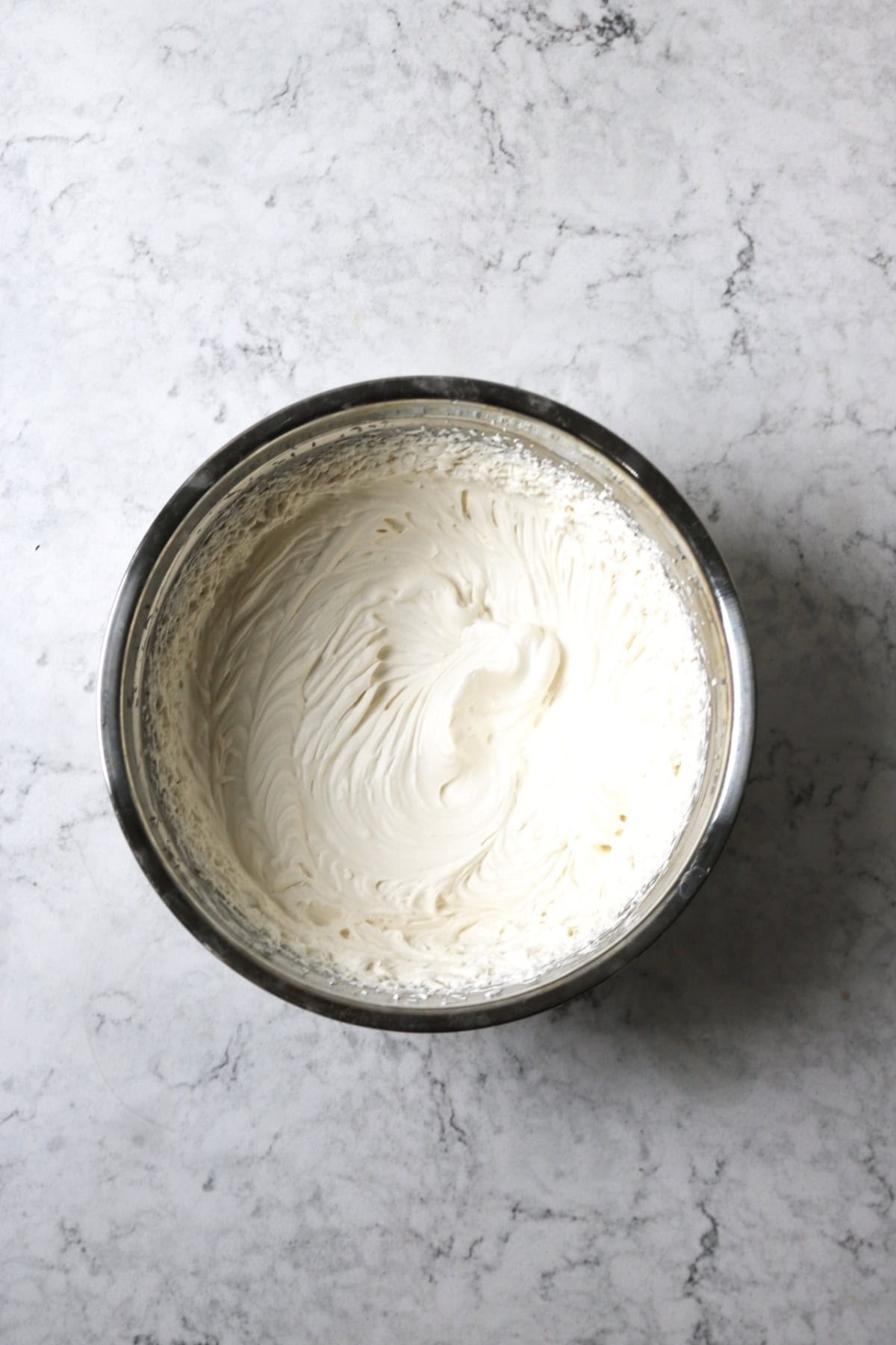 A metal mixing bowl containing whipped vegan cheesecake filling