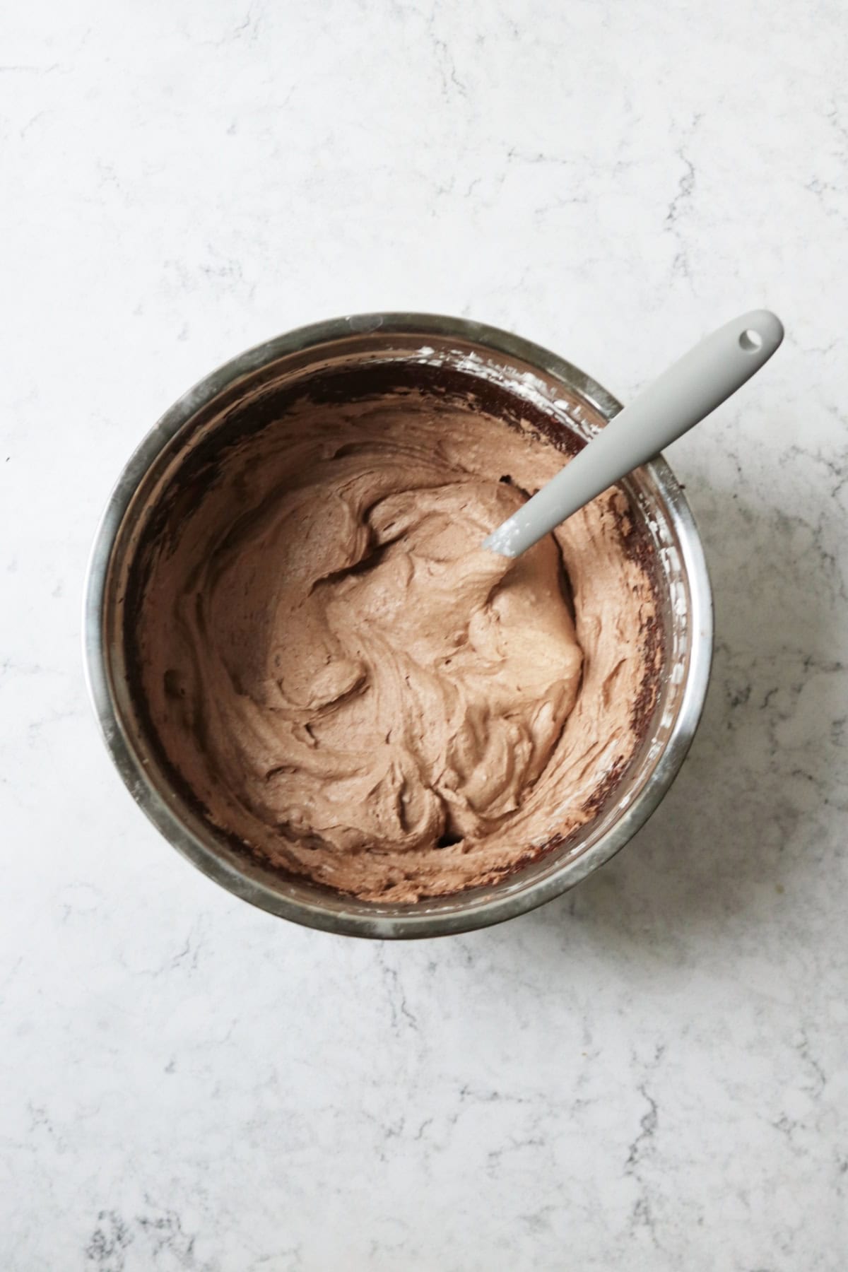 A metal mixing bowl filled with whipped vegan chocolate cheesecake filling and a grey spatula