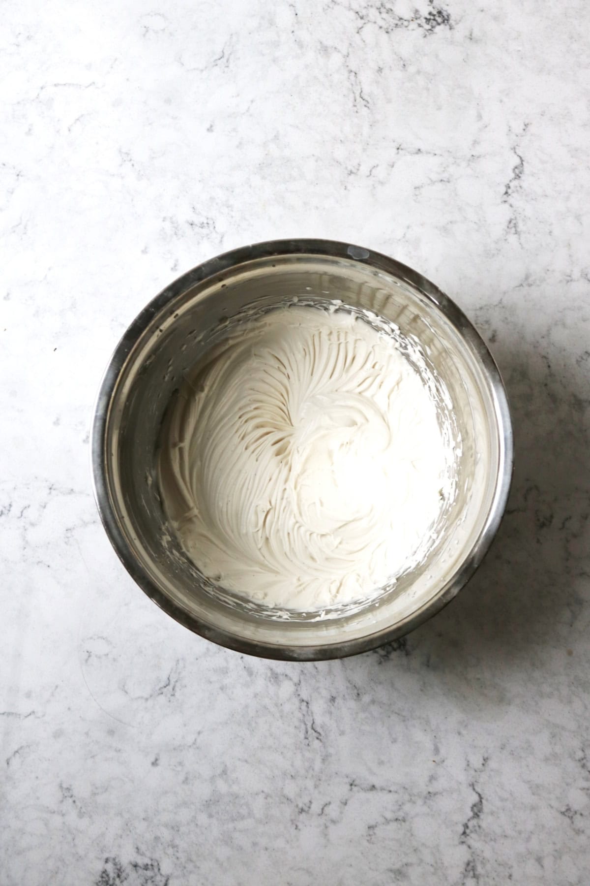 A metal mixing bowl filled with whipped vegan cream cheese, icing sugar and vanilla paste