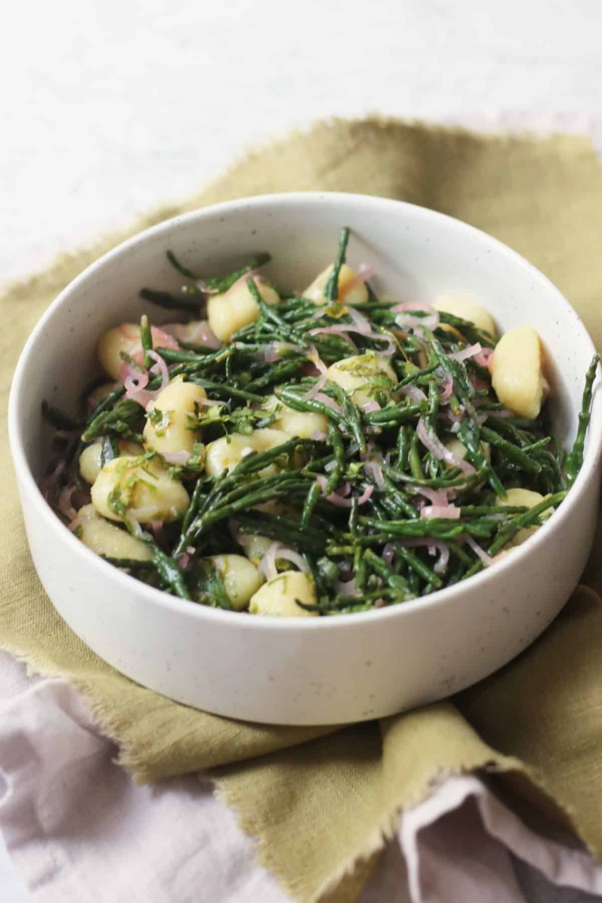 A bowl of Vegan Samphire Gnocchi served in a white bowl with a green napkin