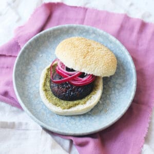 A BBQ Portobello Mushroom Burger in a bun with pesto and pickled red onion rings
