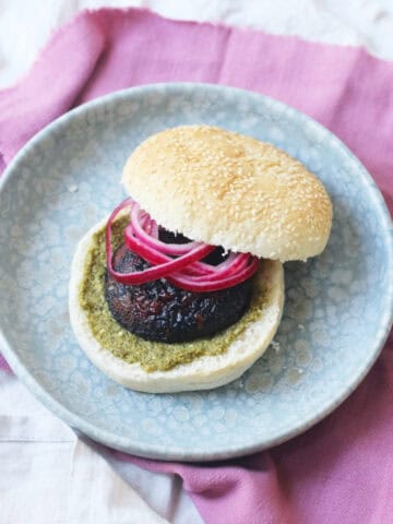 A BBQ Portobello Mushroom Burger in a bun with pesto and pickled red onion rings