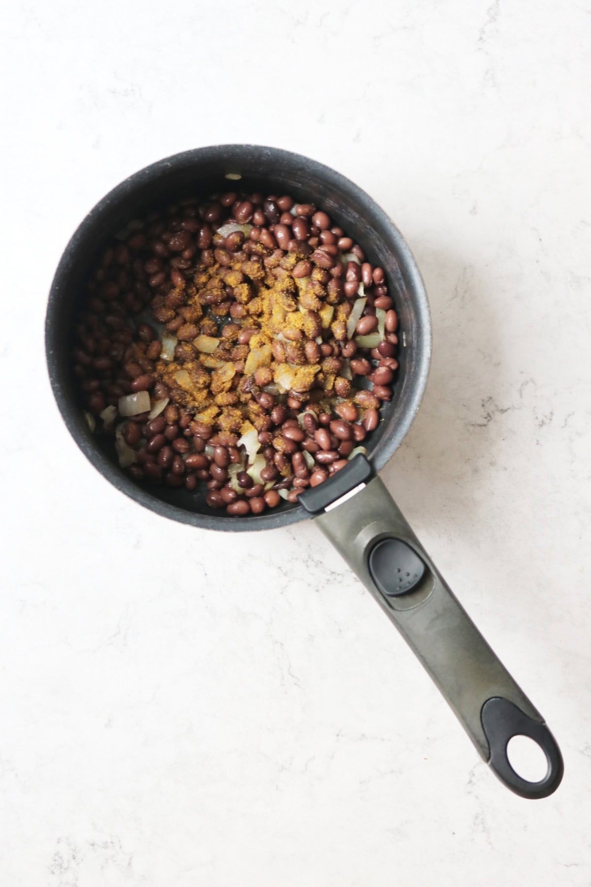 Black beans cooking in a saucepan with ground spices and onion