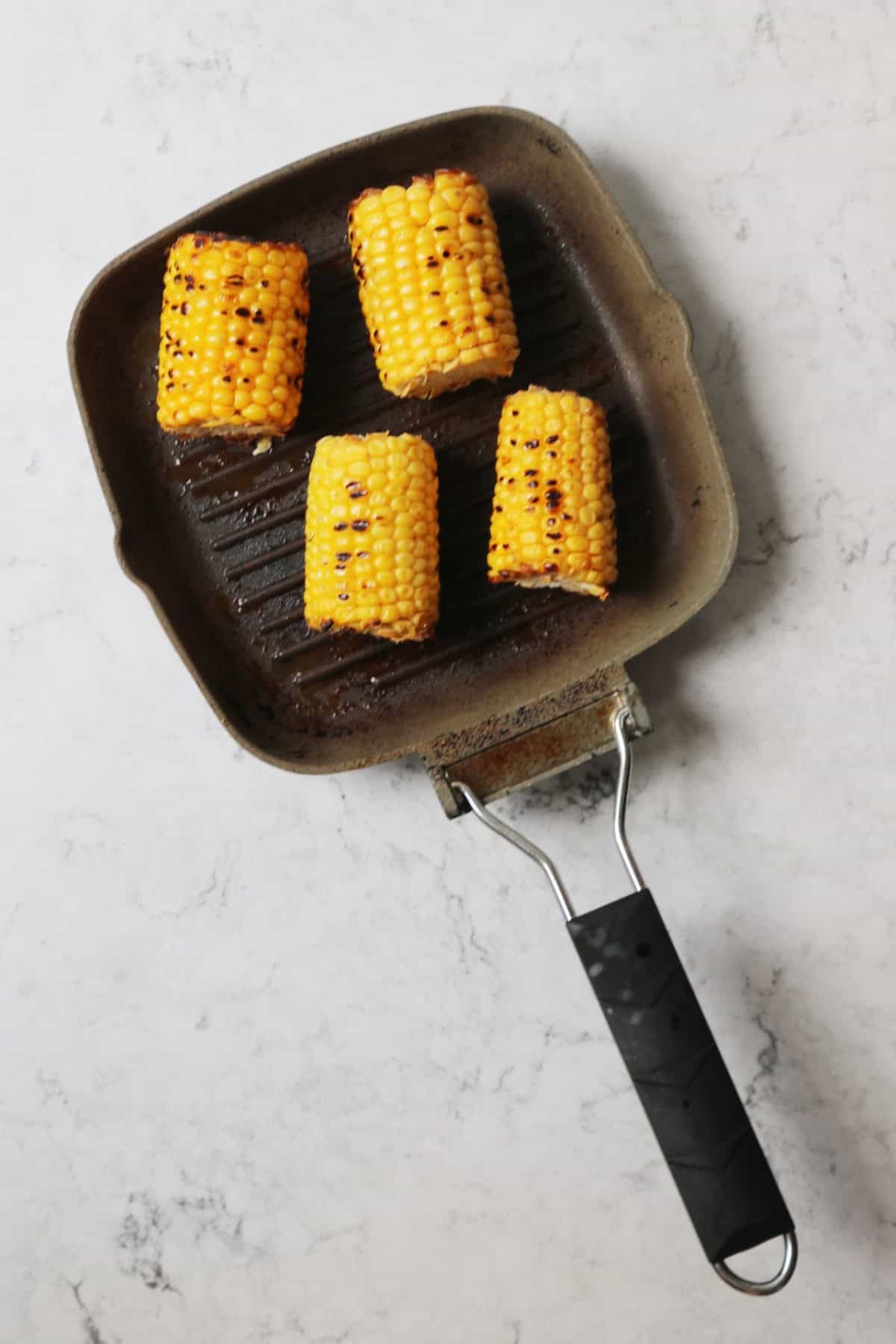 4 corn on the cobs cooking in a griddle pan with black char marks