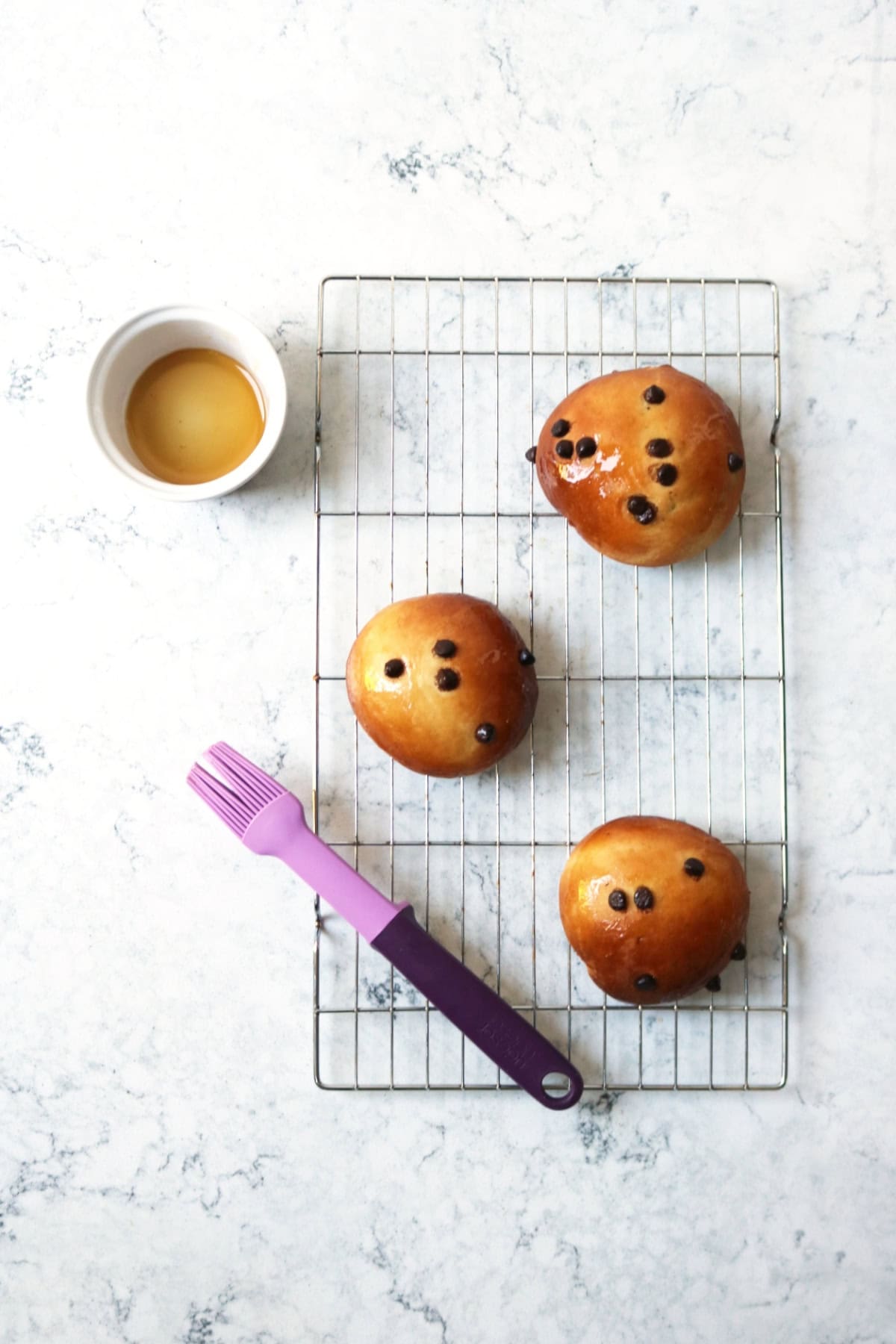 3 Vegan Chocolate Maritozzi buns on a wire rack being glazed with maple syrup