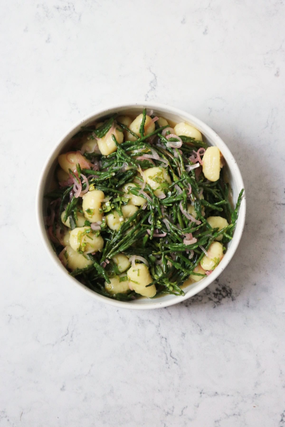 A bowl of Vegan Samphire Gnocchi served in a white bowl on a white marble countertop