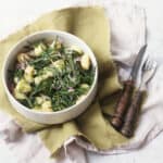 A bowl of Vegan Samphire Gnocchi served in a white bowl with a green napkin and wooden handled knife and fork