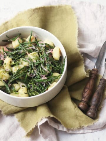 A bowl of Vegan Samphire Gnocchi served in a white bowl with a green napkin and wooden handled knife and fork