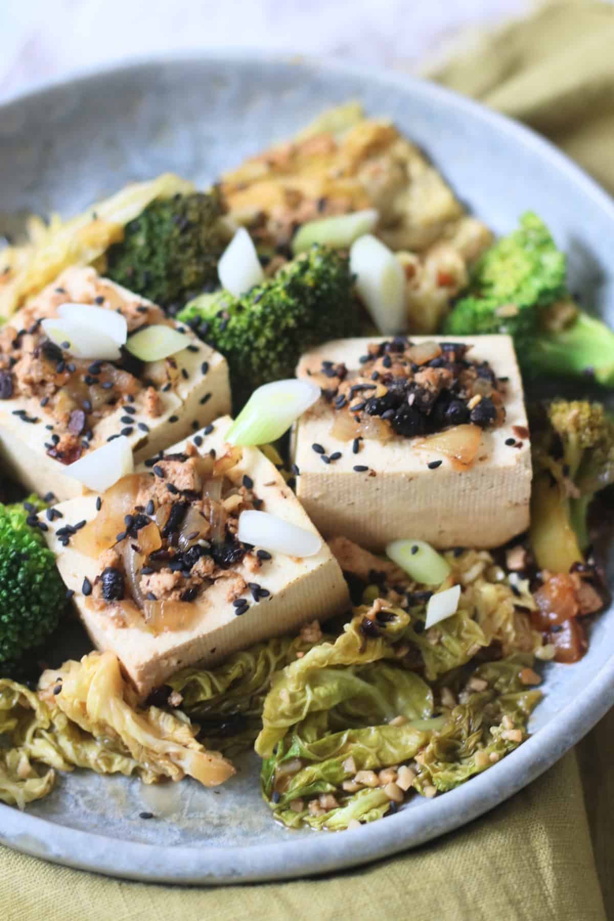 3 pieces of Braised Black Bean Stuffed Tofu served with cabbage and broccoli on a plate with a green napkin