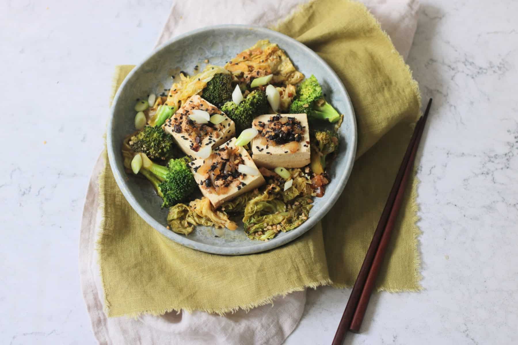 3 pieces of Braised Black Bean Stuffed Tofu served with cabbage and broccoli on a plate with a green napkin and wooden chopsticks