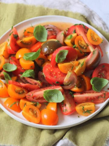 A Gremolata Topped Tomato Salad served on a white platter on top of a green napkin.