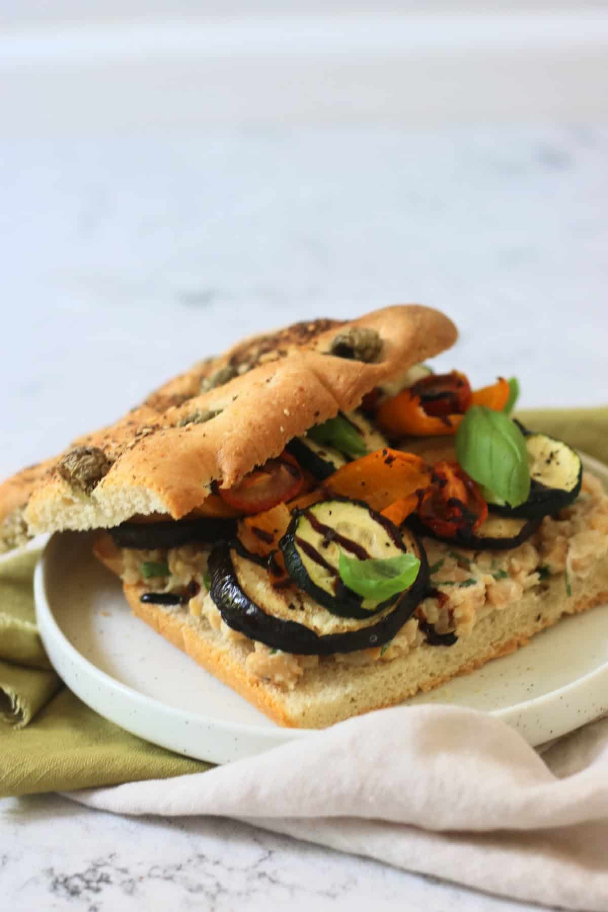 A Roasted Vegetable and Chickpea Focaccia Sandwich with the top slice of bread slightly askew showing the filling underneath