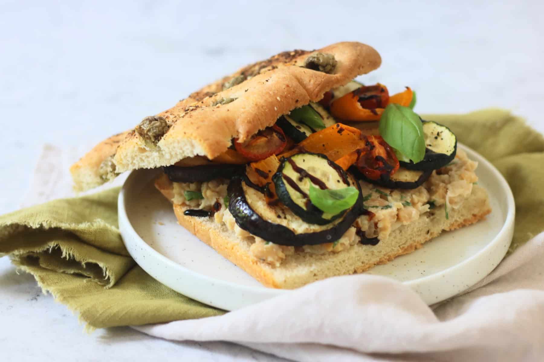 A Roasted Vegetable and Chickpea Focaccia Sandwich with the top slice of bread slightly askew showing the filling underneath