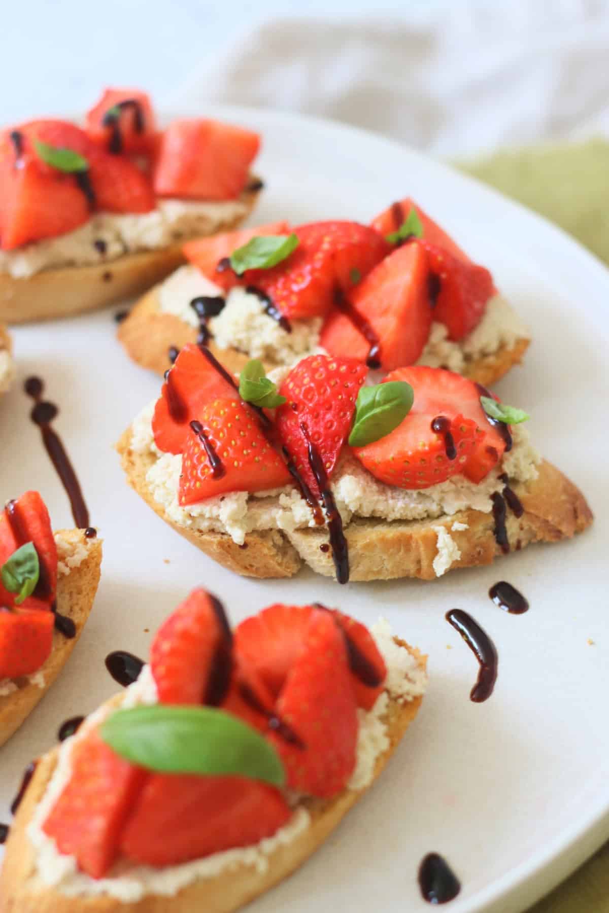 A close up of a Vegan Ricotta and Strawberry Crostini that has been drizzled with balsamic glaze and topped with basil leaves.