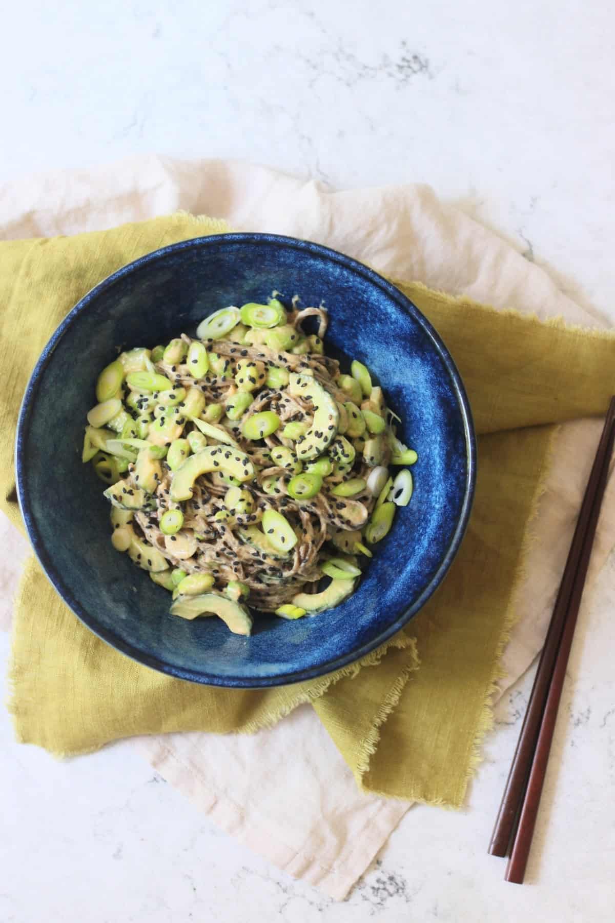 A bowl of Cold Sesame and Peanut Soba Noodles served with a green napkin and two wooden chopsticks