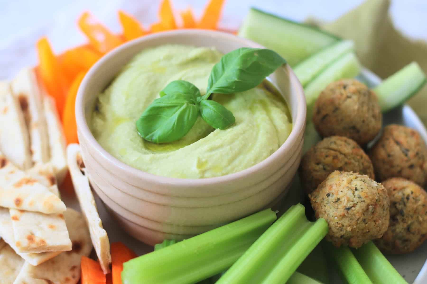 A crudites platter made up of pitta, carrots, celery, falafel, cucumber and orange pepper with a bowl of Roasted Garlic and Basil Hummus