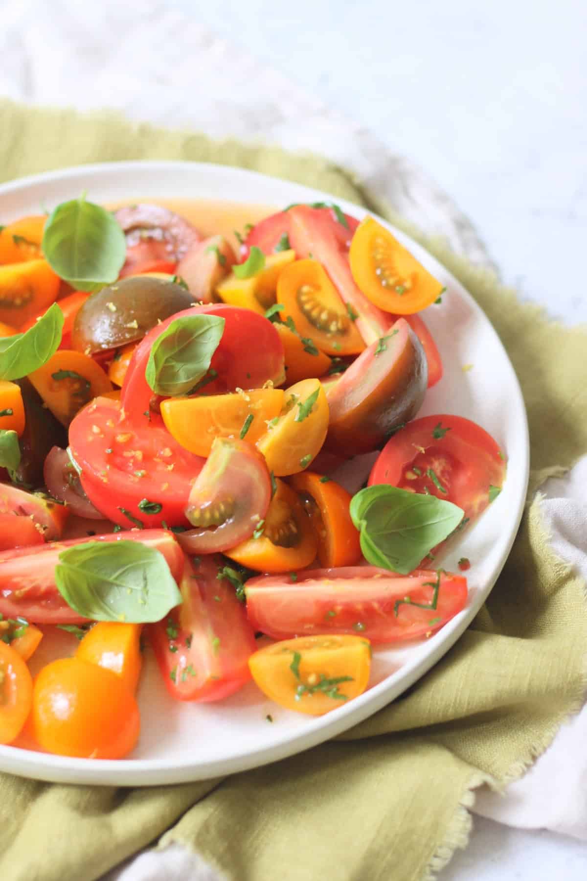 A Gremolata Topped Tomato Salad served on a white platter on top of a green napkin.