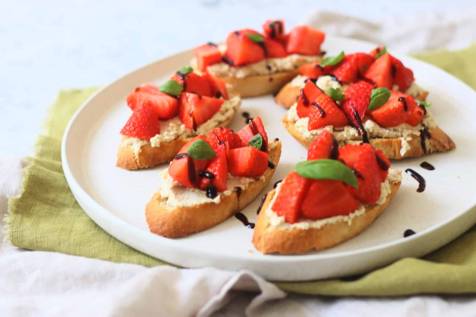 6 Vegan Ricotta and Strawberry Crostini served on a white plate on top of a green napkin.