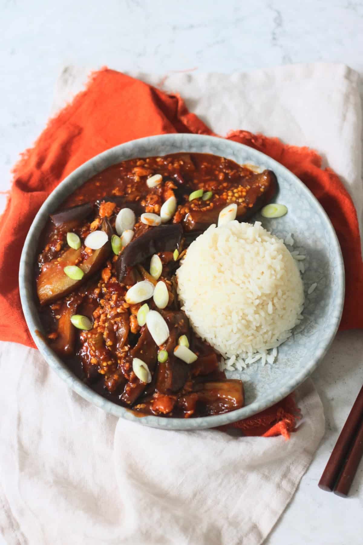 Vegan Sichuan Style Braised Aubergines topped with sliced spring onions and served with white rice