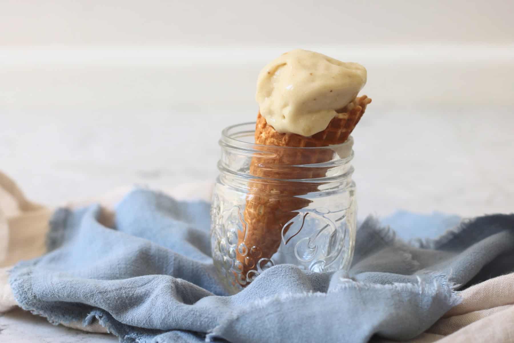 A waffle ice cream cone topped with Vegan Banana and Coconut Ice Cream resting in a glass jar