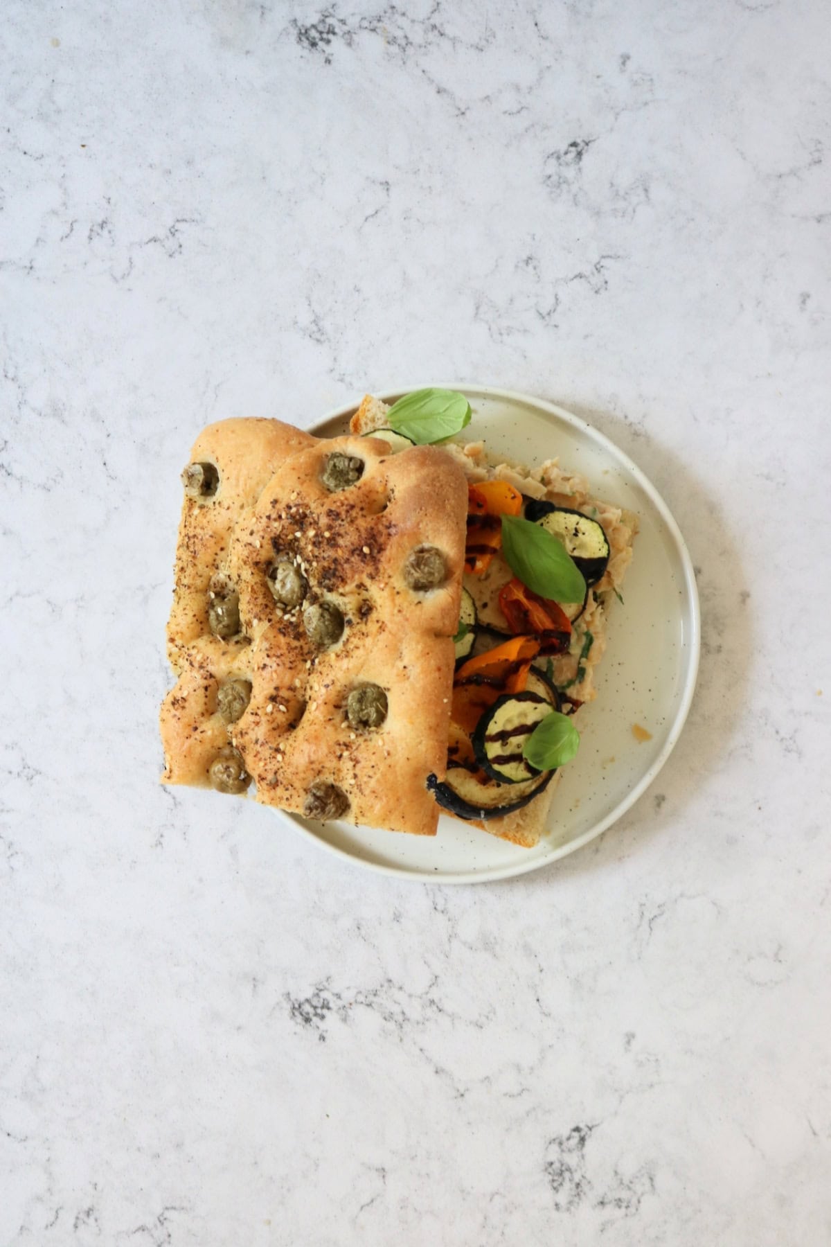 A Roasted Vegetable and Chickpea Focaccia Sandwich with the top slice of bread slightly askew showing the filling underneath