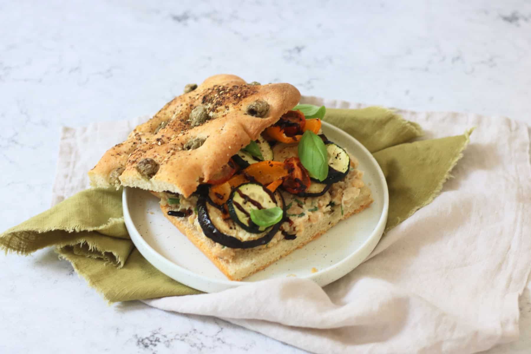 A Roasted Vegetable and Chickpea Focaccia Sandwich with the top slice of bread slightly askew showing the filling underneath