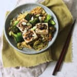 3 pieces of Braised Black Bean Stuffed Tofu served with cabbage and broccoli on a plate with a green napkin and wooden chopsticks