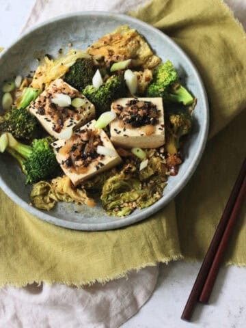 3 pieces of Braised Black Bean Stuffed Tofu served with cabbage and broccoli on a plate with a green napkin and wooden chopsticks