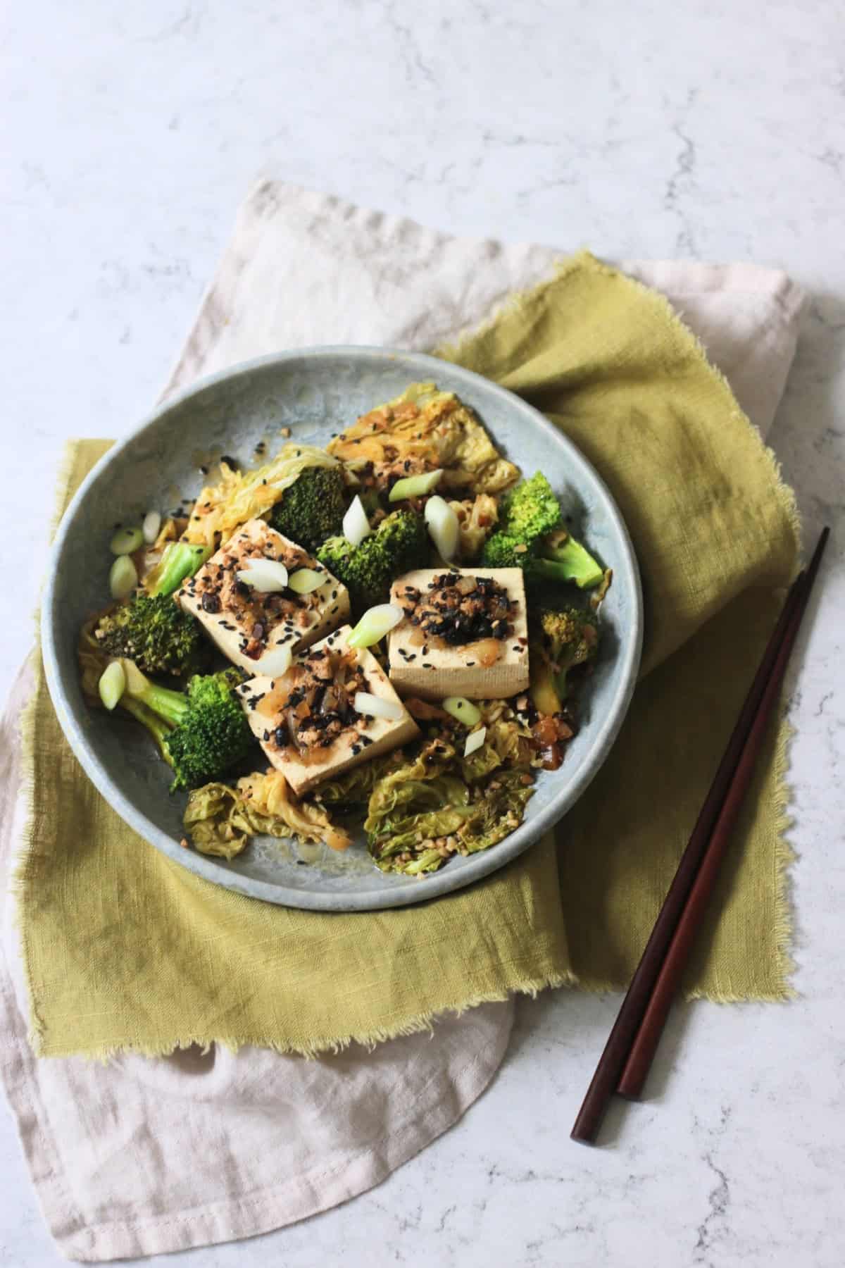3 pieces of Braised Black Bean Stuffed Tofu served with cabbage and broccoli on a plate with a green napkin and wooden chopsticks