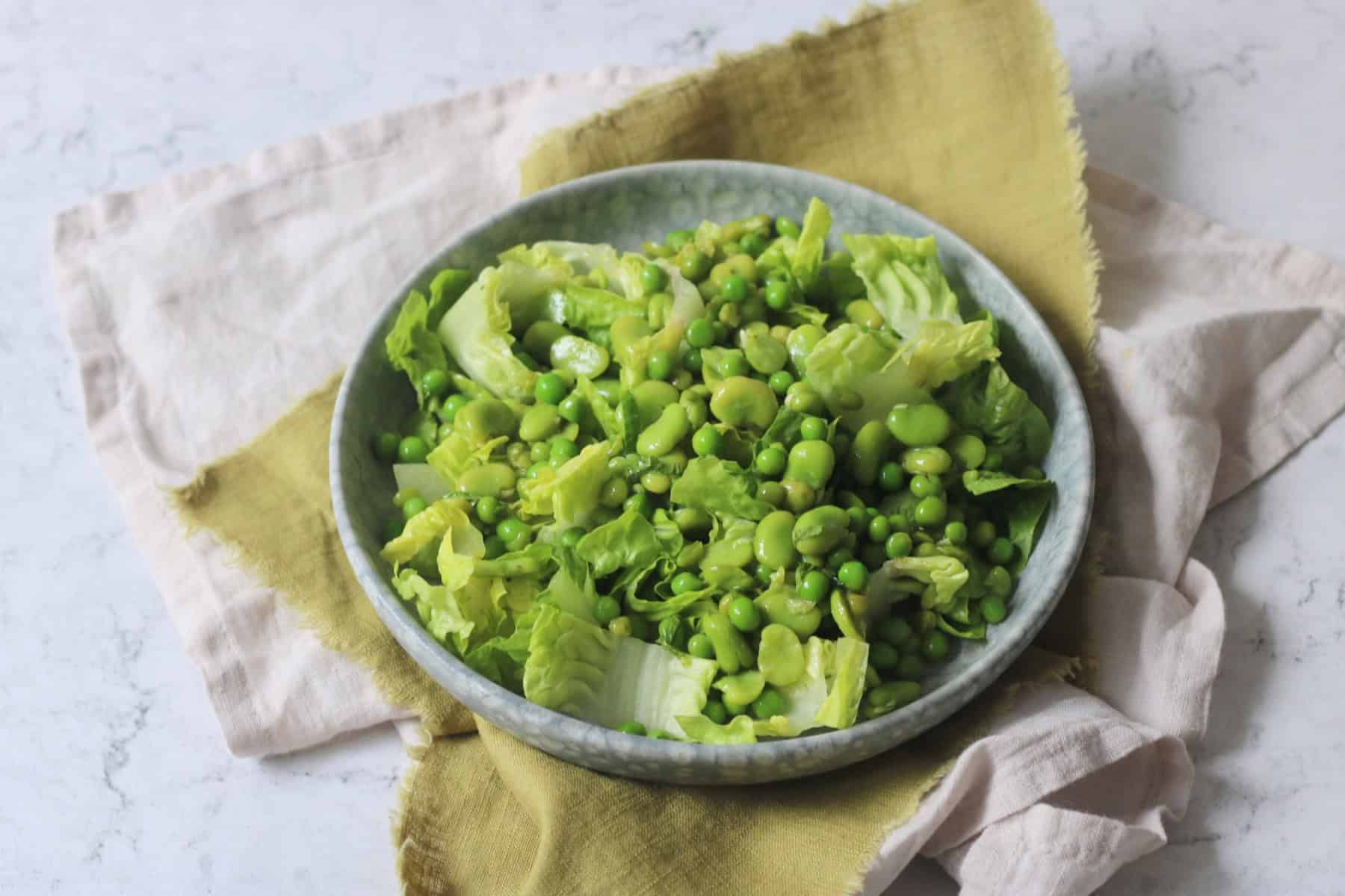 Pea and Broad Bean Salad with Little Gem Lettuce and Fresh Mint dressed with Dijon Mustard Dressing served on a light blue plate on top of a green napkin.