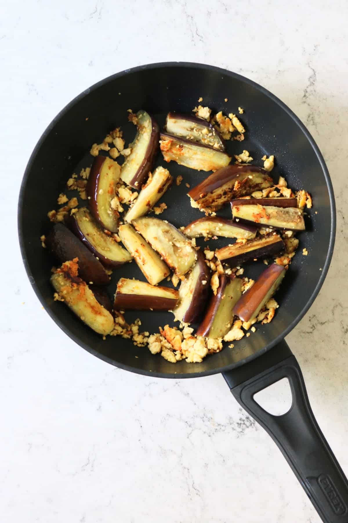 Browning aubergines along with crumbled tofu in a large flat bottomed frying pan