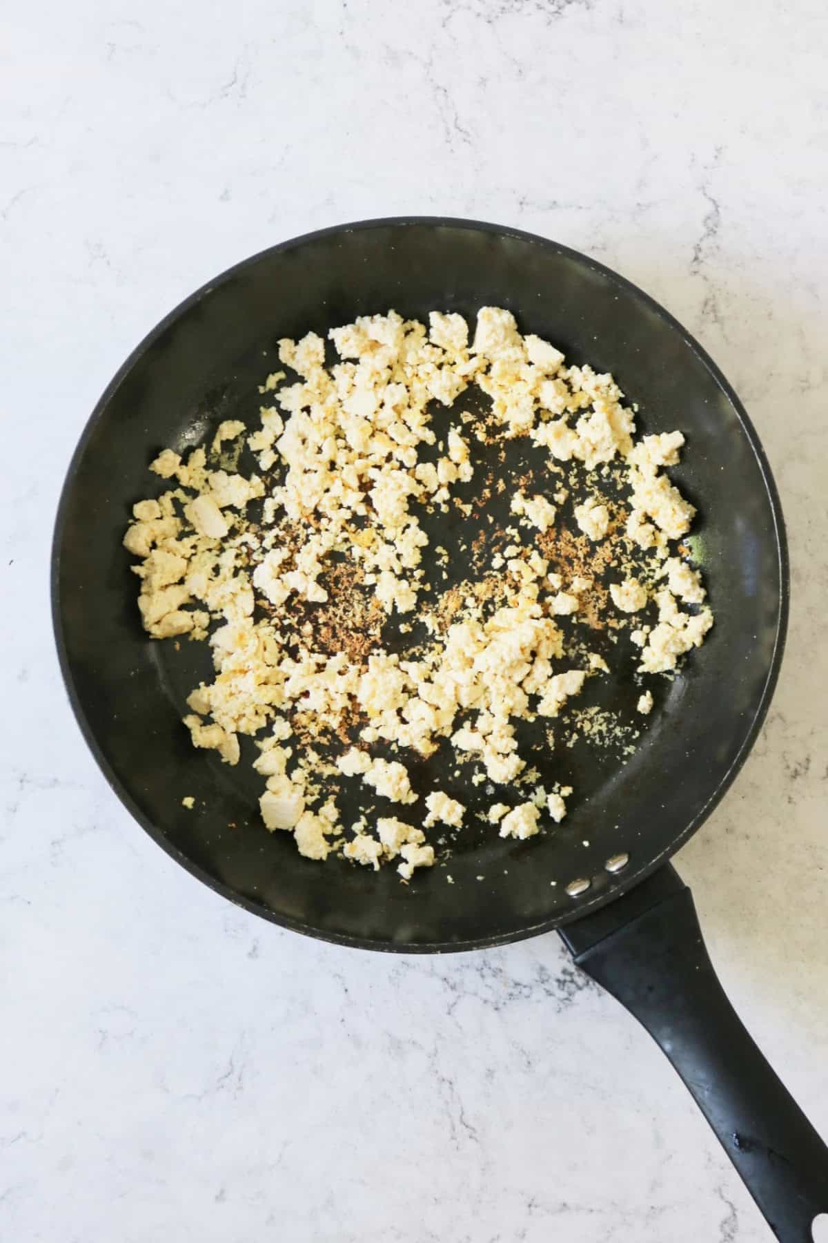 Crumbled tofu being browned in a large flat bottomed frying pan