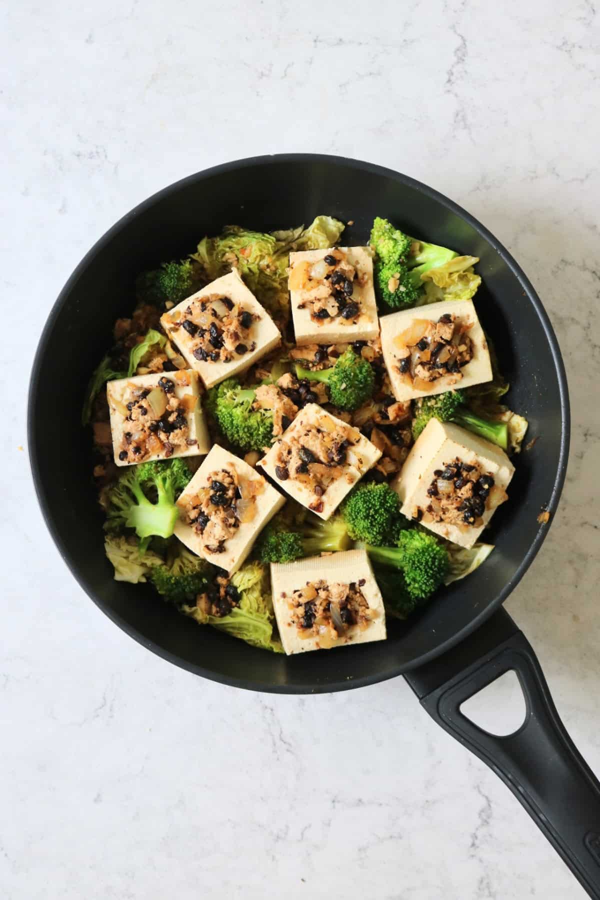 Braised Black Bean Stuffed Tofu served with cabbage and broccoli cooking in a large flat bottomed frying pan