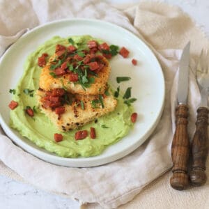 A plate of Crispy Lemon Pepper Tofu with Creamy Avocado Sauce and Bacon Crunch with fresh parsley and a wooden handled knife and fork.