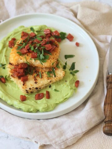 A plate of Crispy Lemon Pepper Tofu with Creamy Avocado Sauce and Bacon Crunch with fresh parsley and a wooden handled knife and fork.