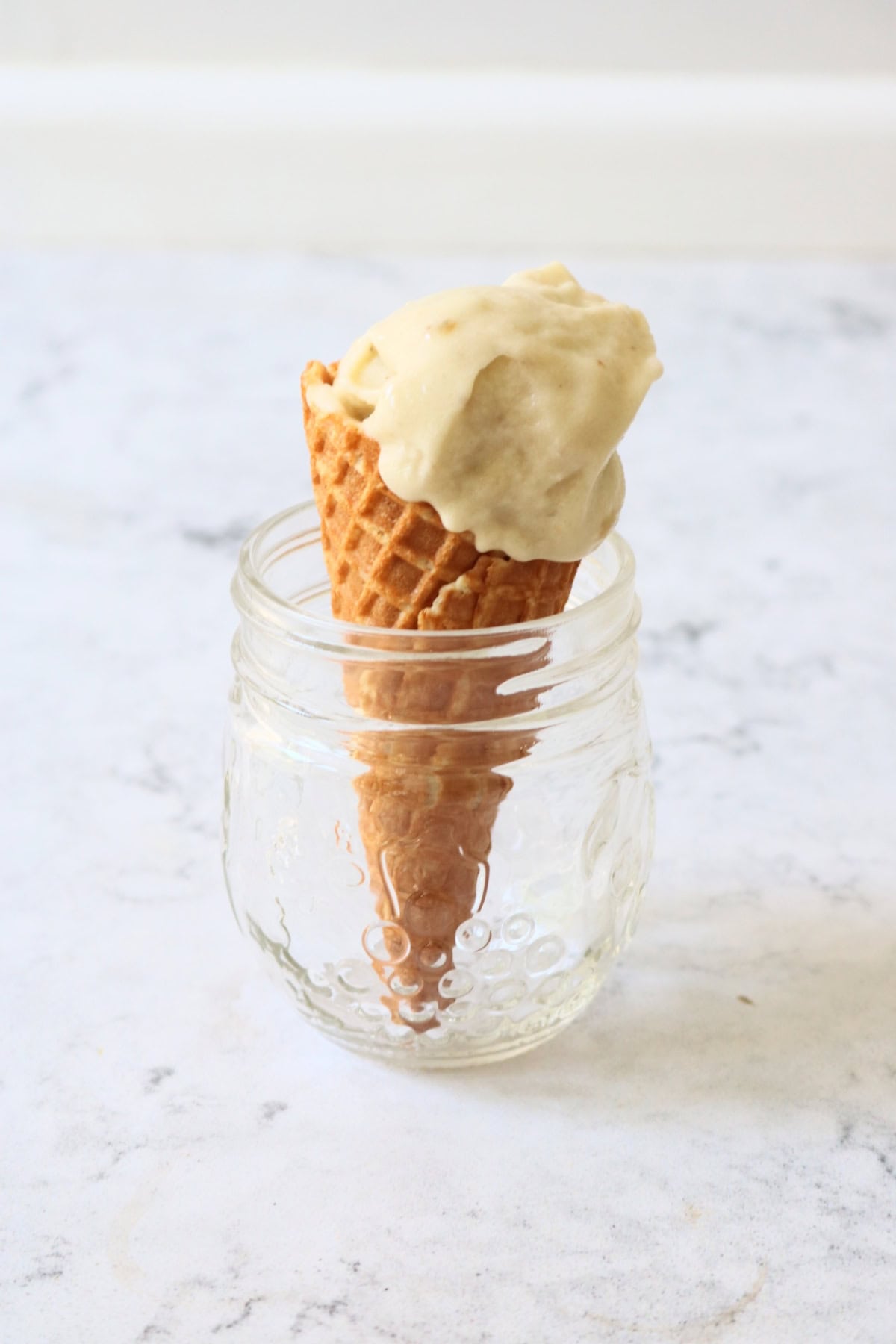 A waffle ice cream cone topped with Vegan Banana and Coconut Ice Cream resting in a glass jar