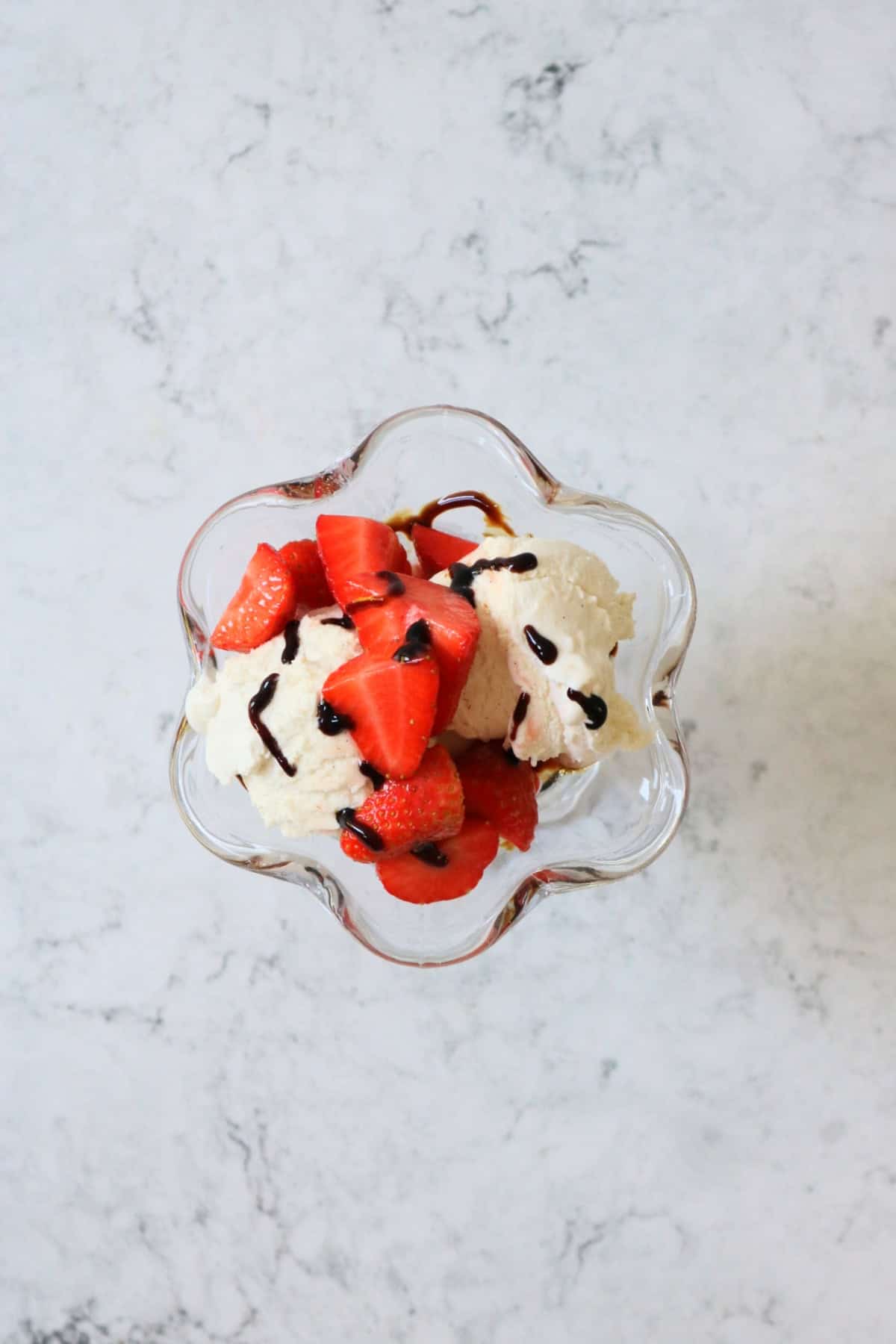 Dairy free ice cream topped with strawberries and balsamic glaze in an ice cream sundae glass