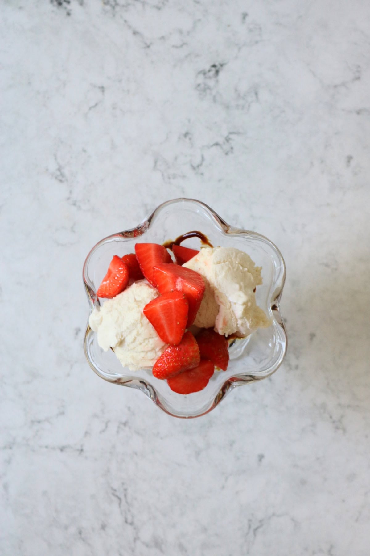 Dairy free ice cream topped with macerated strawberries in an ice cream sundae glass