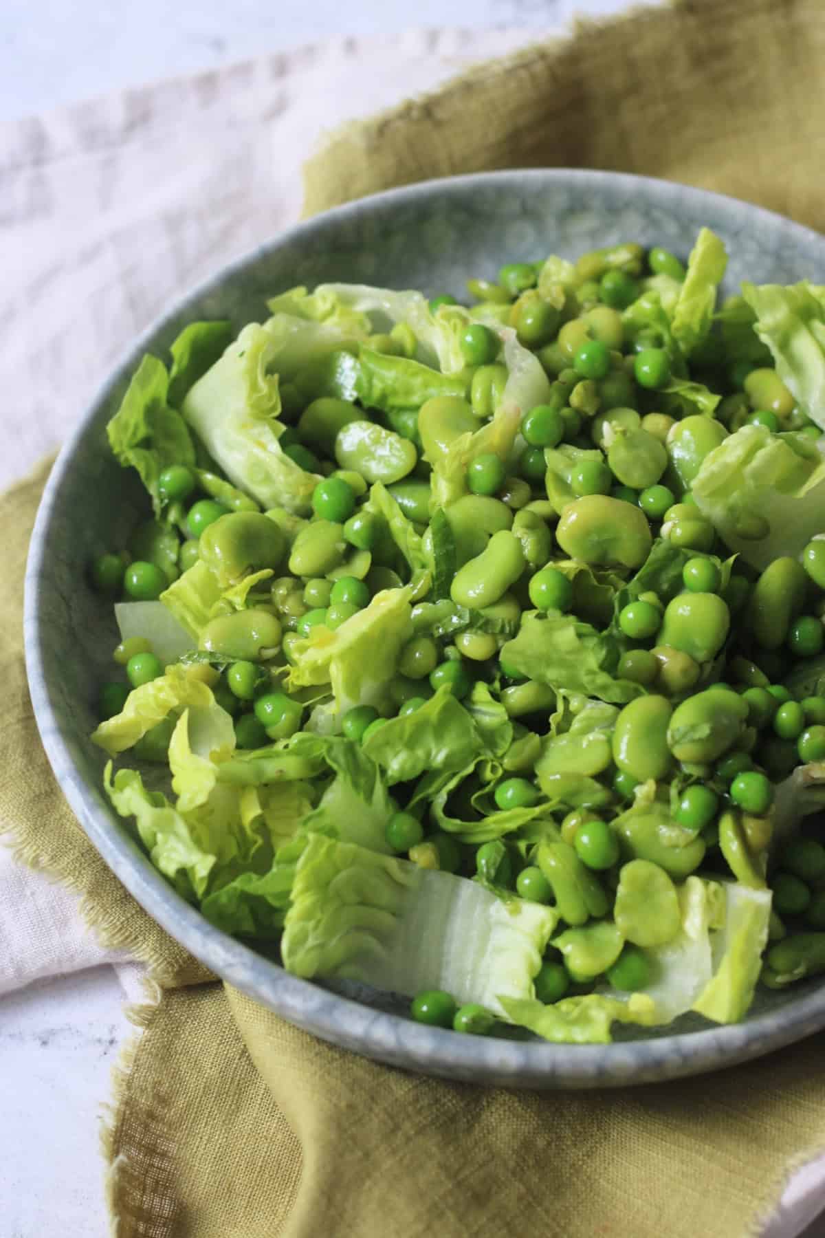 Pea and Broad Bean Salad with Little Gem Lettuce and Fresh Mint dressed with Dijon Mustard Dressing served on a light blue plate on top of a green napkin.