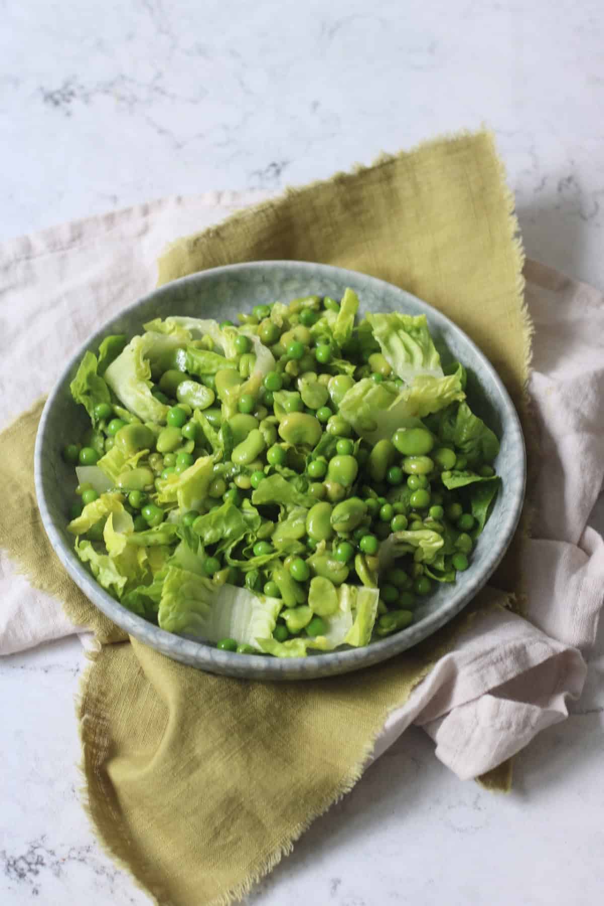 Pea and Broad Bean Salad with Little Gem Lettuce and Fresh Mint dressed with Dijon Mustard Dressing served on a light blue plate on top of a green napkin.