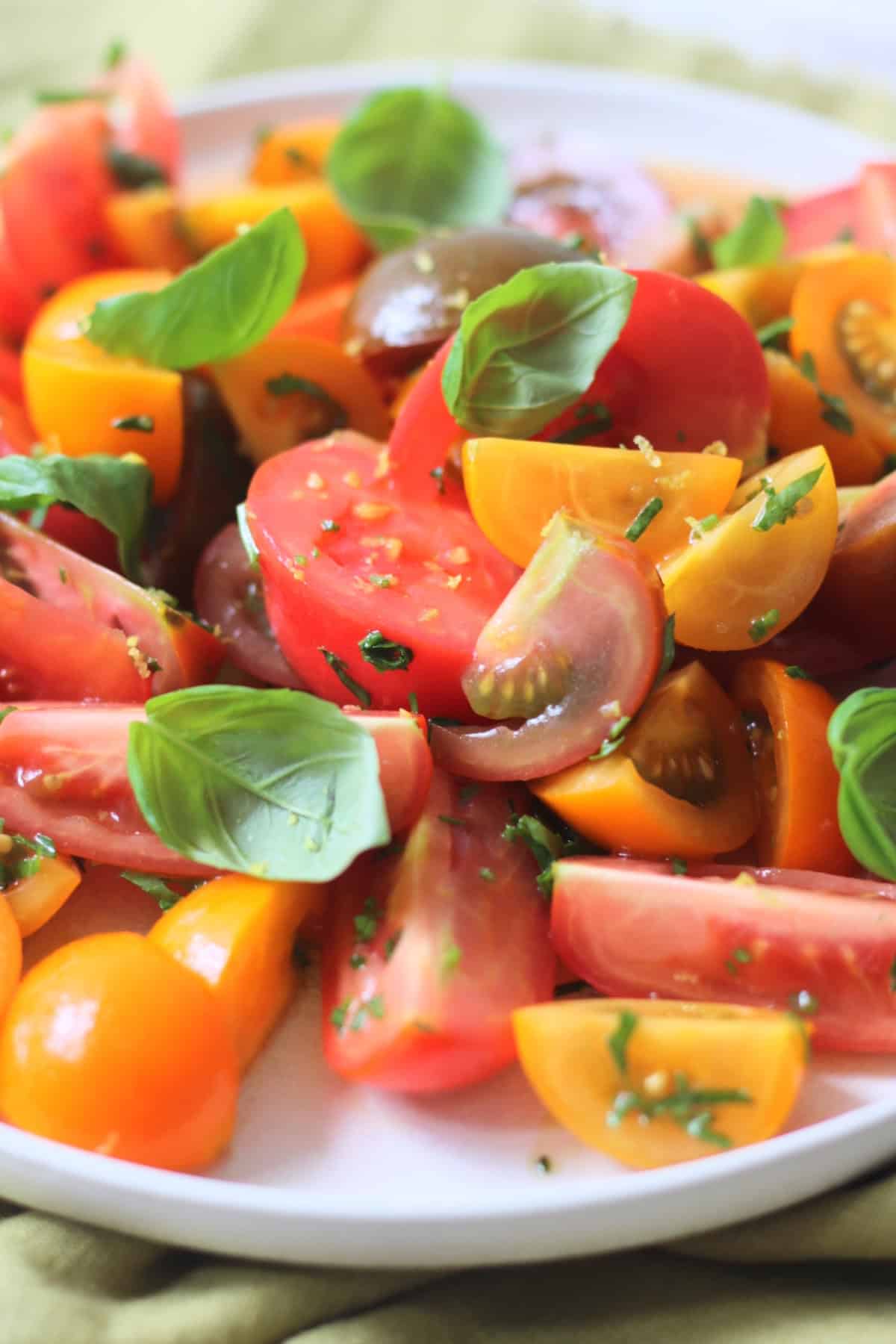 A Gremolata Topped Tomato Salad served on a white platter on top of a green napkin.