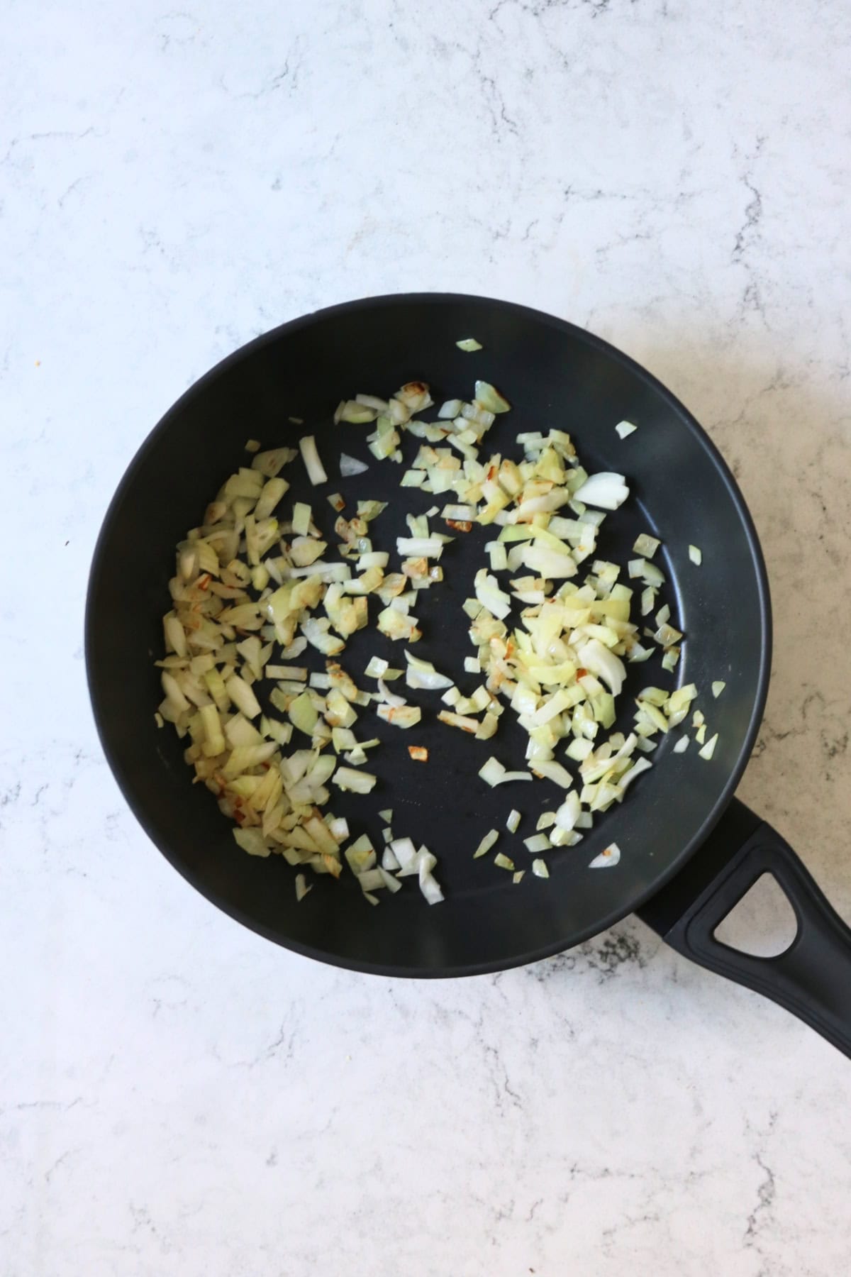 Diced onions frying in a large frying pan