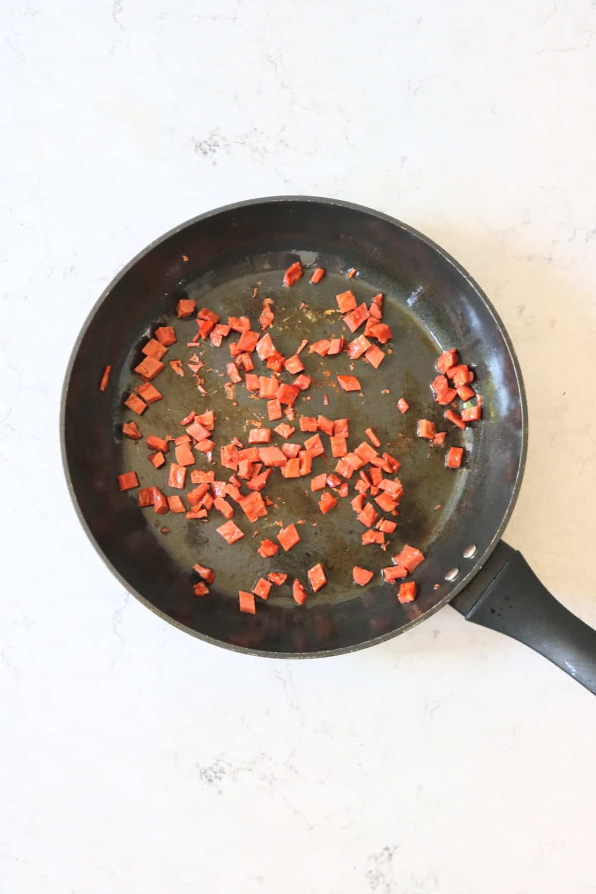 Chopped up vegan bacon pieces frying in a large frying pan