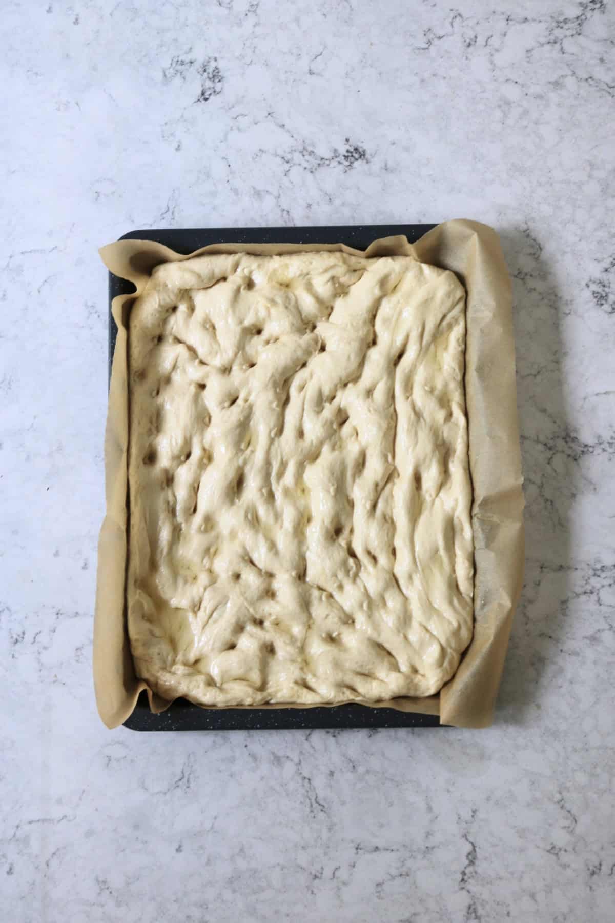 Focaccia dough stretched out over a baking sheet with dimples pressed into the surface