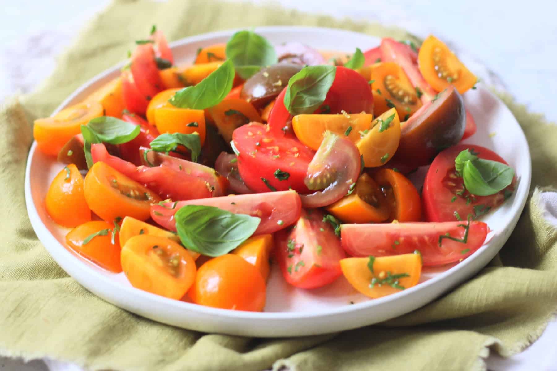 A Gremolata Topped Tomato Salad served on a white platter on top of a green napkin.